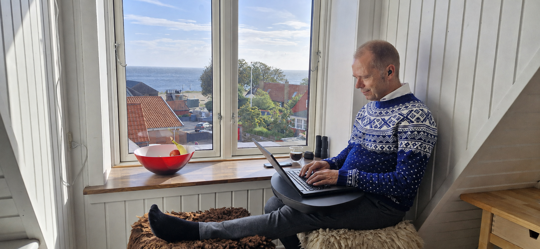 David Hav arbejder med bærbar computer og Jabra earbud ved vinduet i Allinge